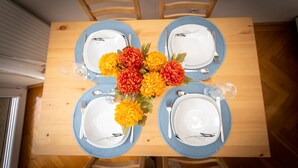 A dining table set for four with blue-rimmed plates, white dinnerware, and a centerpiece of orange and red flowers.