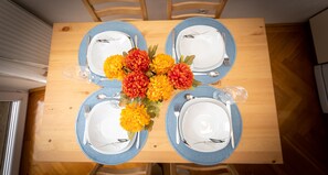 A dining table set for four with blue-rimmed plates, white dinnerware, and a centerpiece of orange and red flowers.