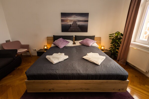 A bedroom with a bed, two pillows, a nightstand, a lamp, a chair, and a plant.