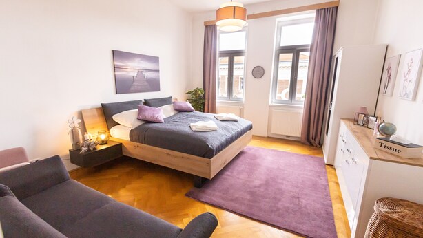 A modern bedroom with a bed, a sofa, a dresser, and a window with curtains.