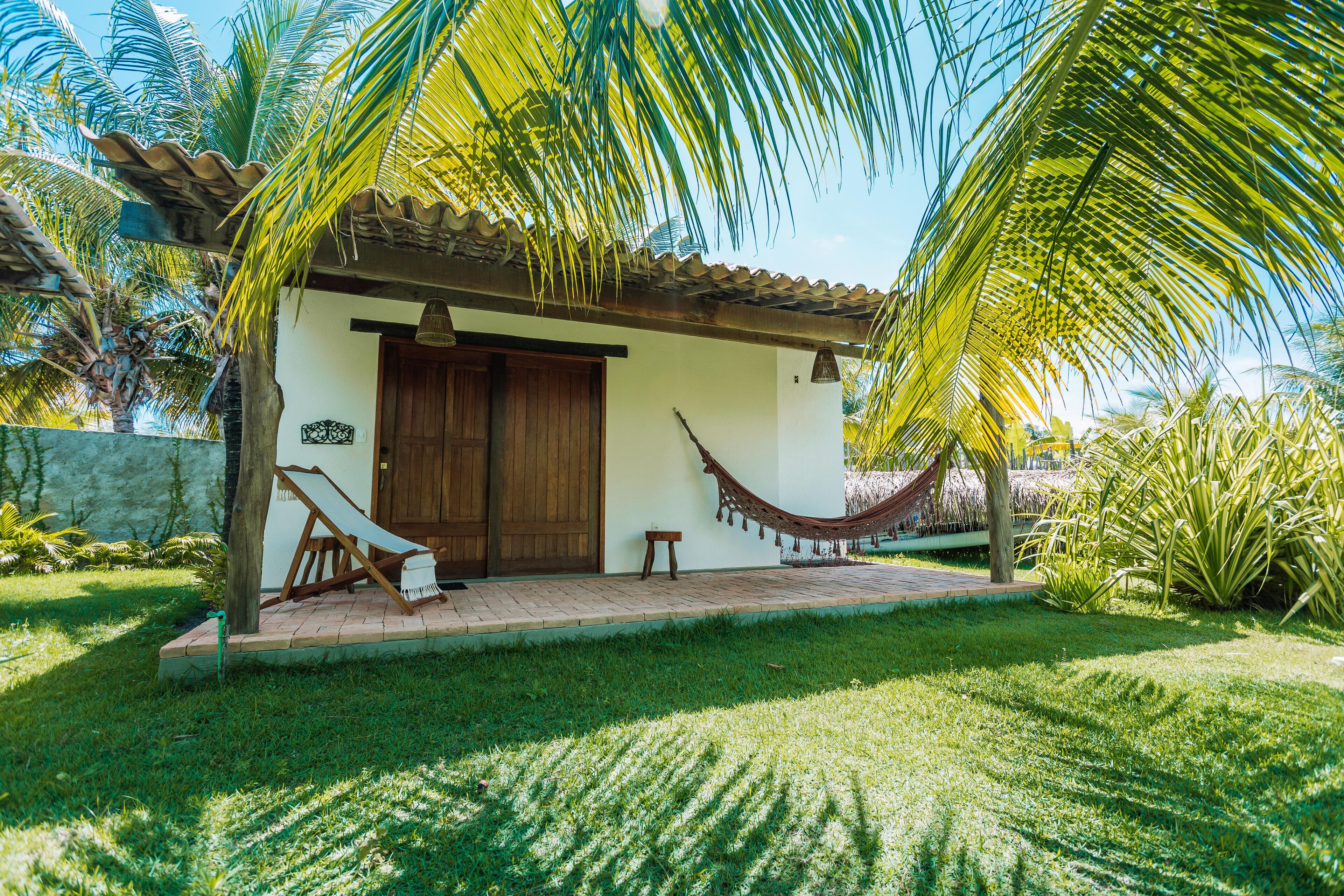 Una casita con puerta de madera, una hamaca y techo de paja.