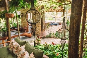 A cozy outdoor seating area with a green sofa, hanging metal lanterns, and lush greenery. - Ocacocar Milagres (São Miguel dos Milagres)
