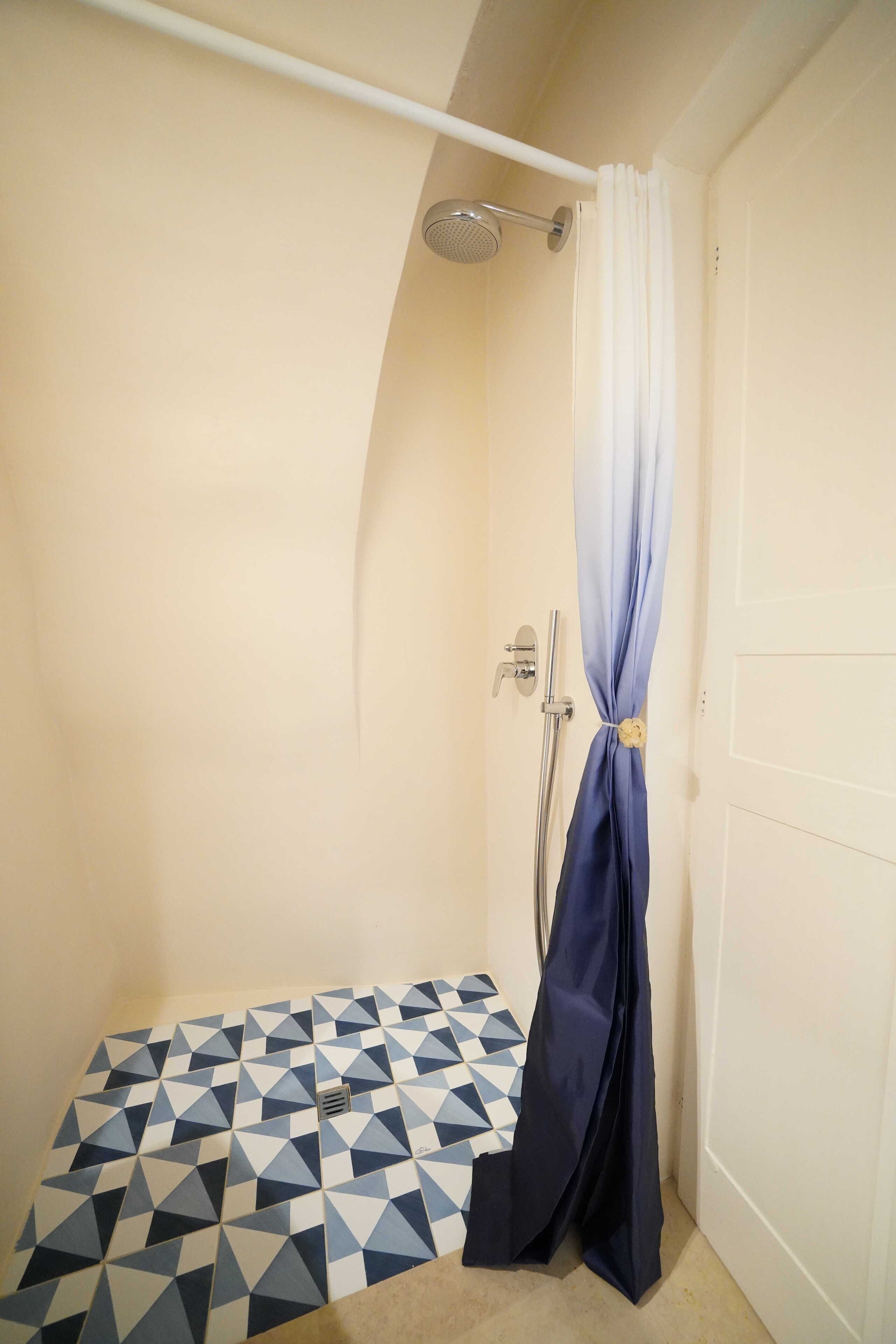 A small bathroom with a shower, a geometric patterned floor, and a white door.