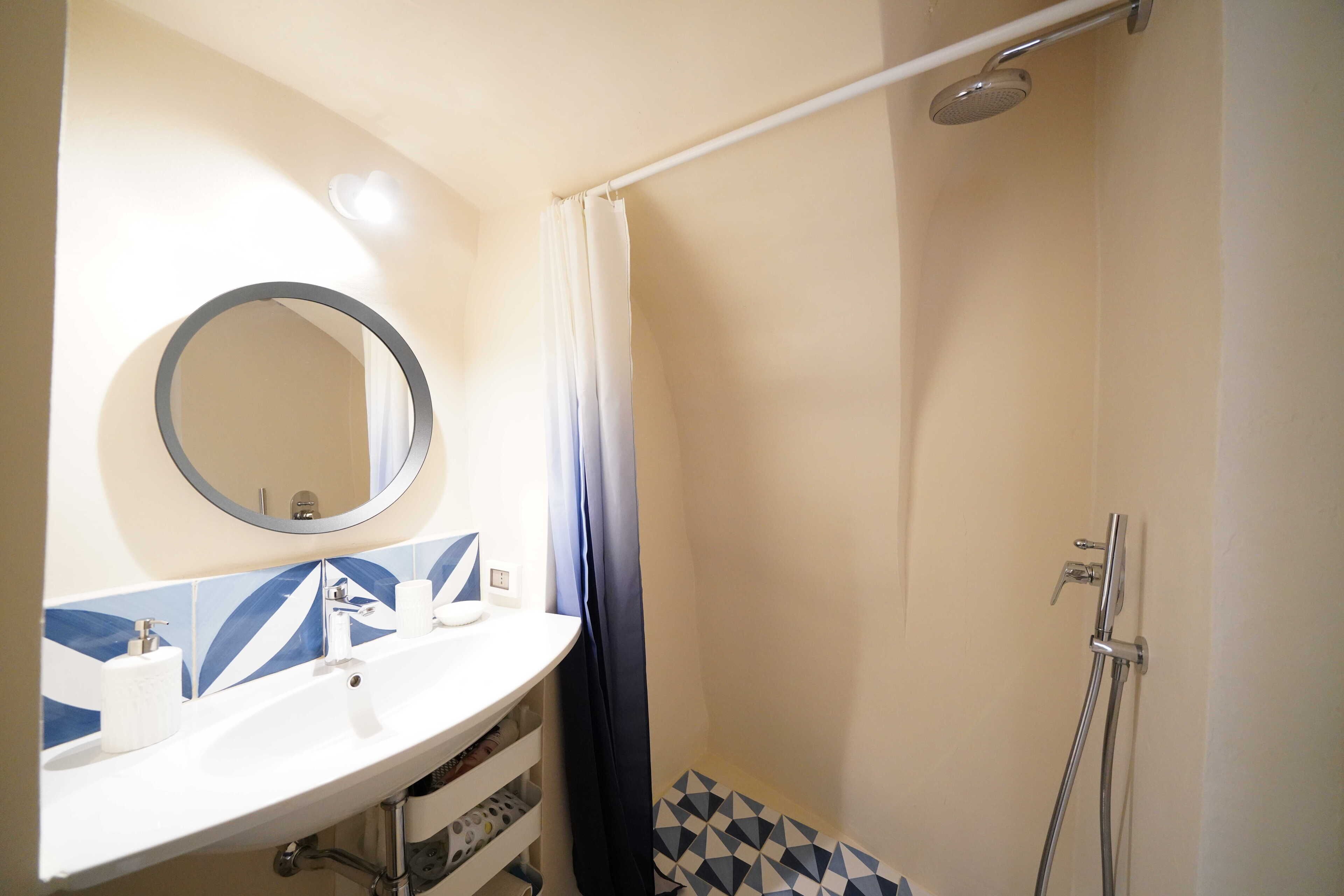 Une salle de bain avec un lavabo blanc, un miroir, une douche avec un rideau et un sol carrelé.