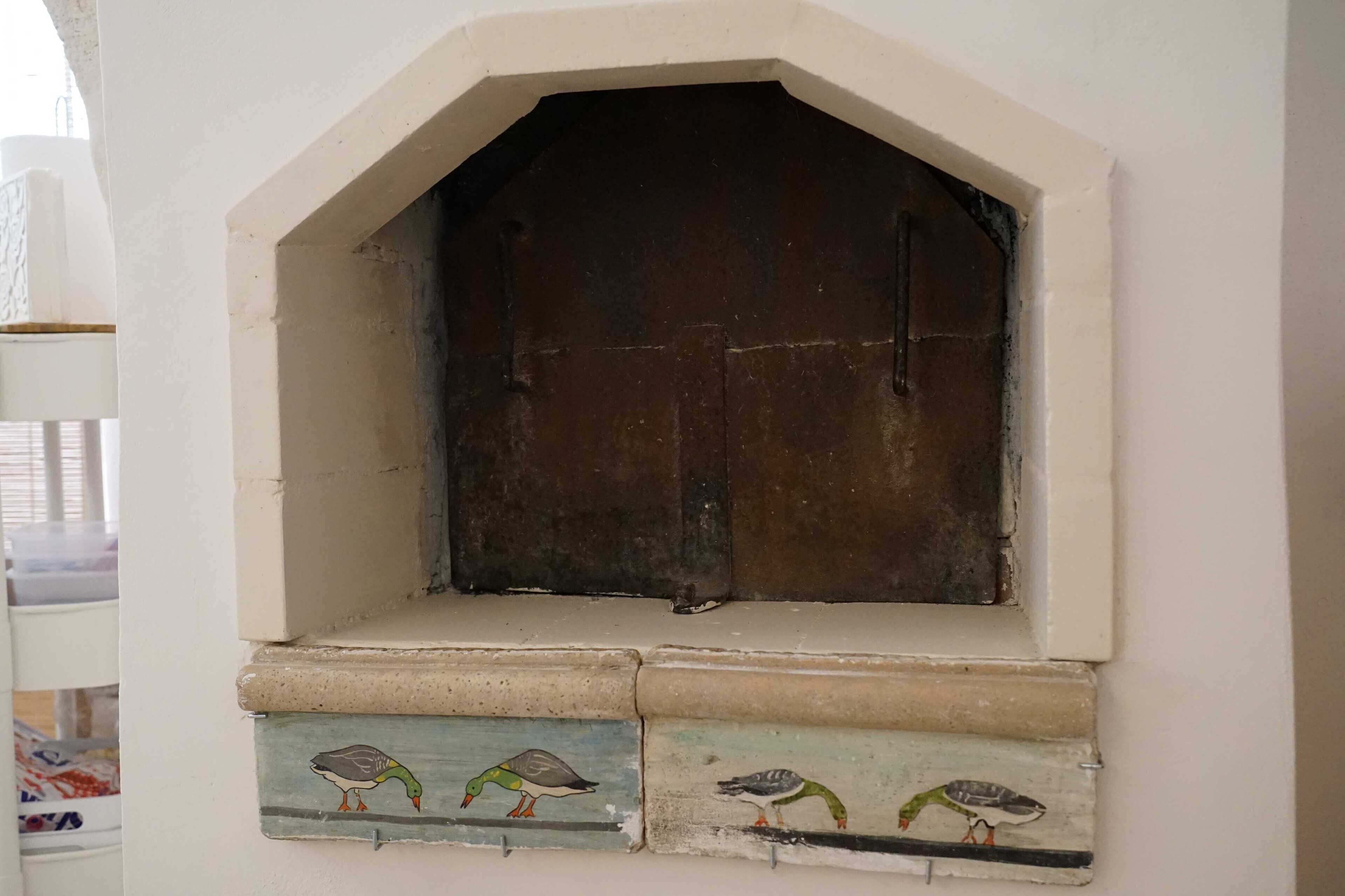 Una petita finestra apuntada amb una porta de fusta, flanquejada per tres rajoles pintades amb representacions d'ocells.