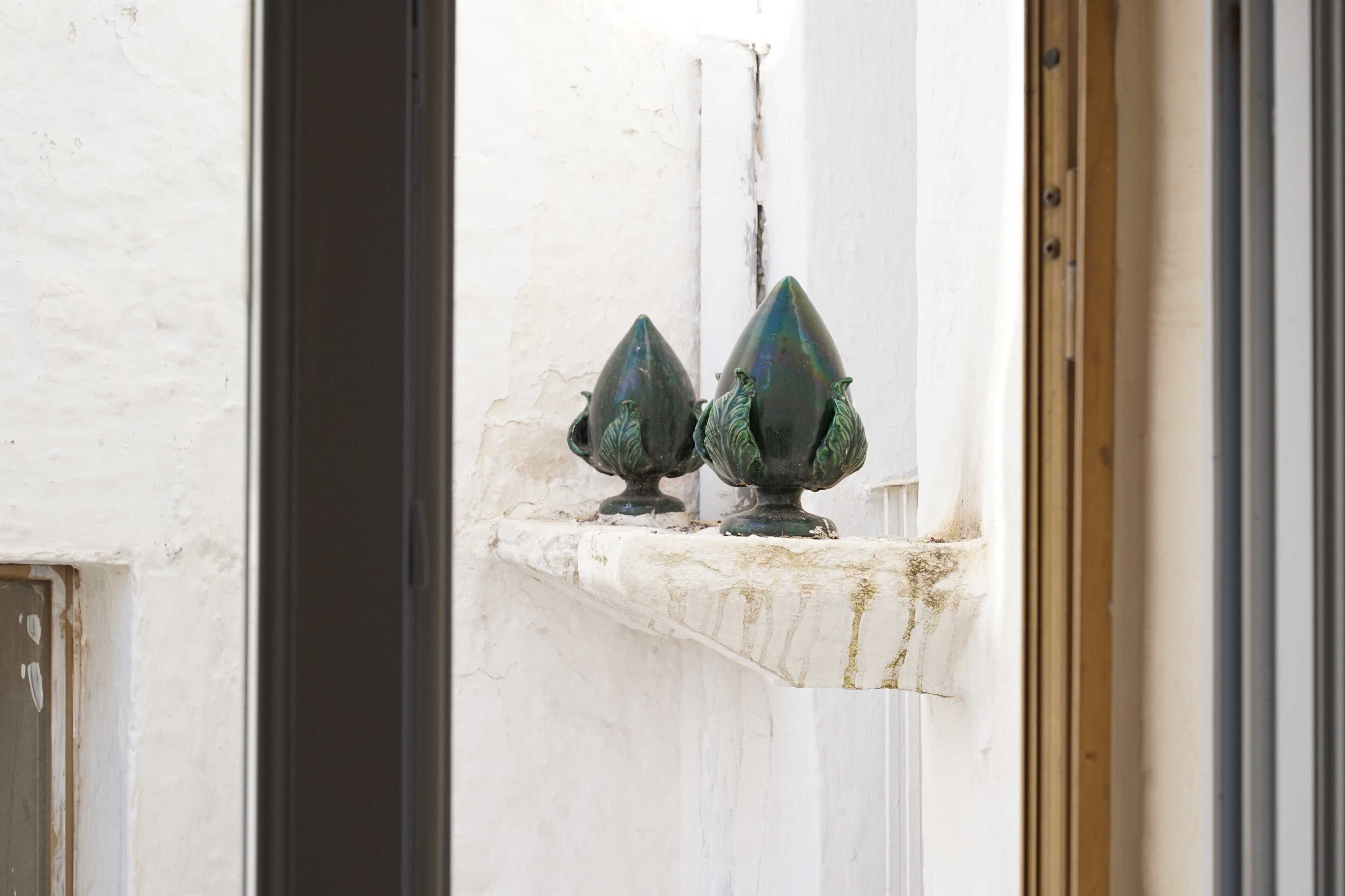 A white wall with two green, pointed objects on a ledge.