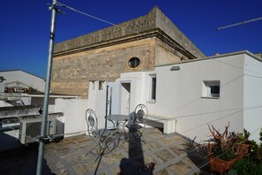 Una terraza en la azotea con una mesa y sillas, una planta en maceta y un edificio con fachada de piedra al fondo.