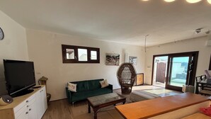 A living room with a television, sofa, chair, and a wooden table. - Sardinian House low cost (frazione brunella)