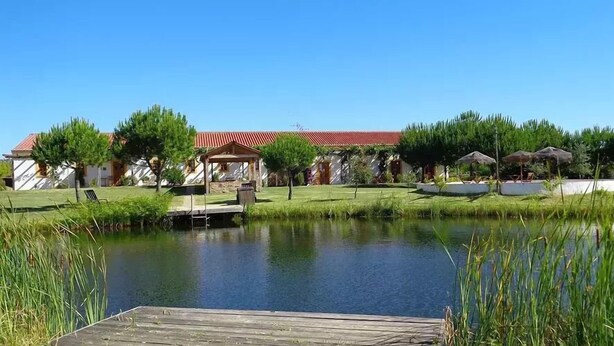 A lakeside view with a wooden dock, a gazebo, and a building with a red roof.