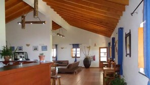 A spacious living area with a wooden ceiling, a bar area, and several potted plants.