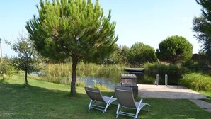 A serene outdoor area with a pond, two metal chairs, a wooden deck, and a tree.
