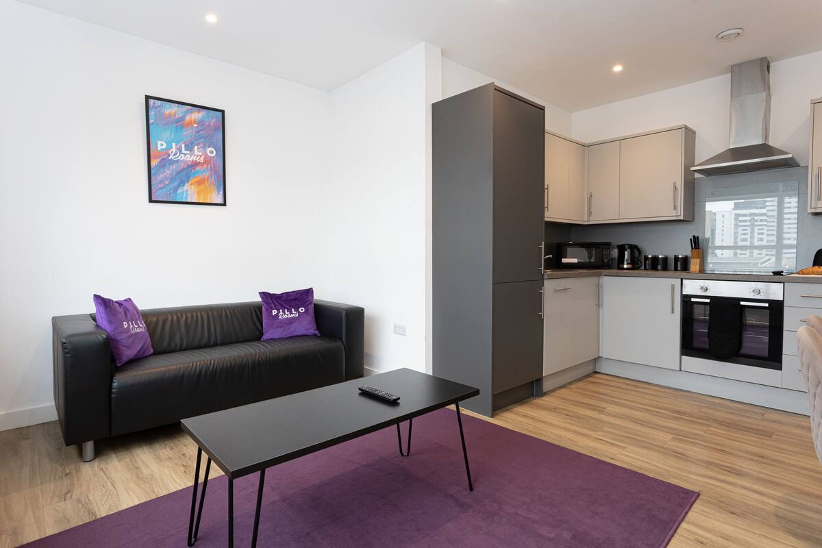 A modern living room with a black sofa, a coffee table, and a purple rug.