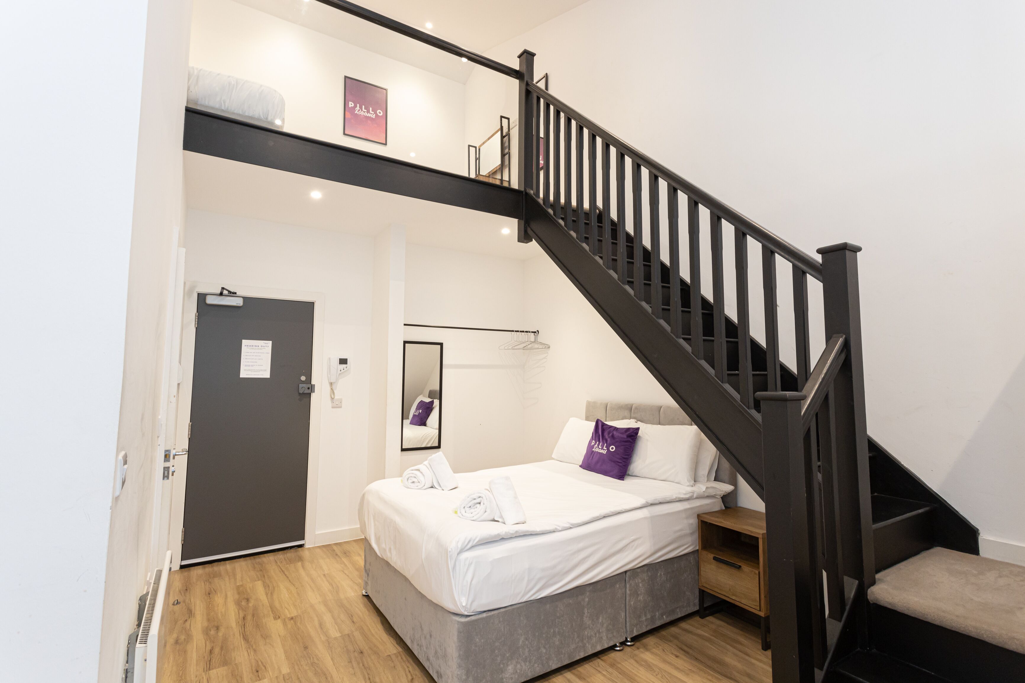 A room with a bed, a dark staircase, a door, and a small wooden table.