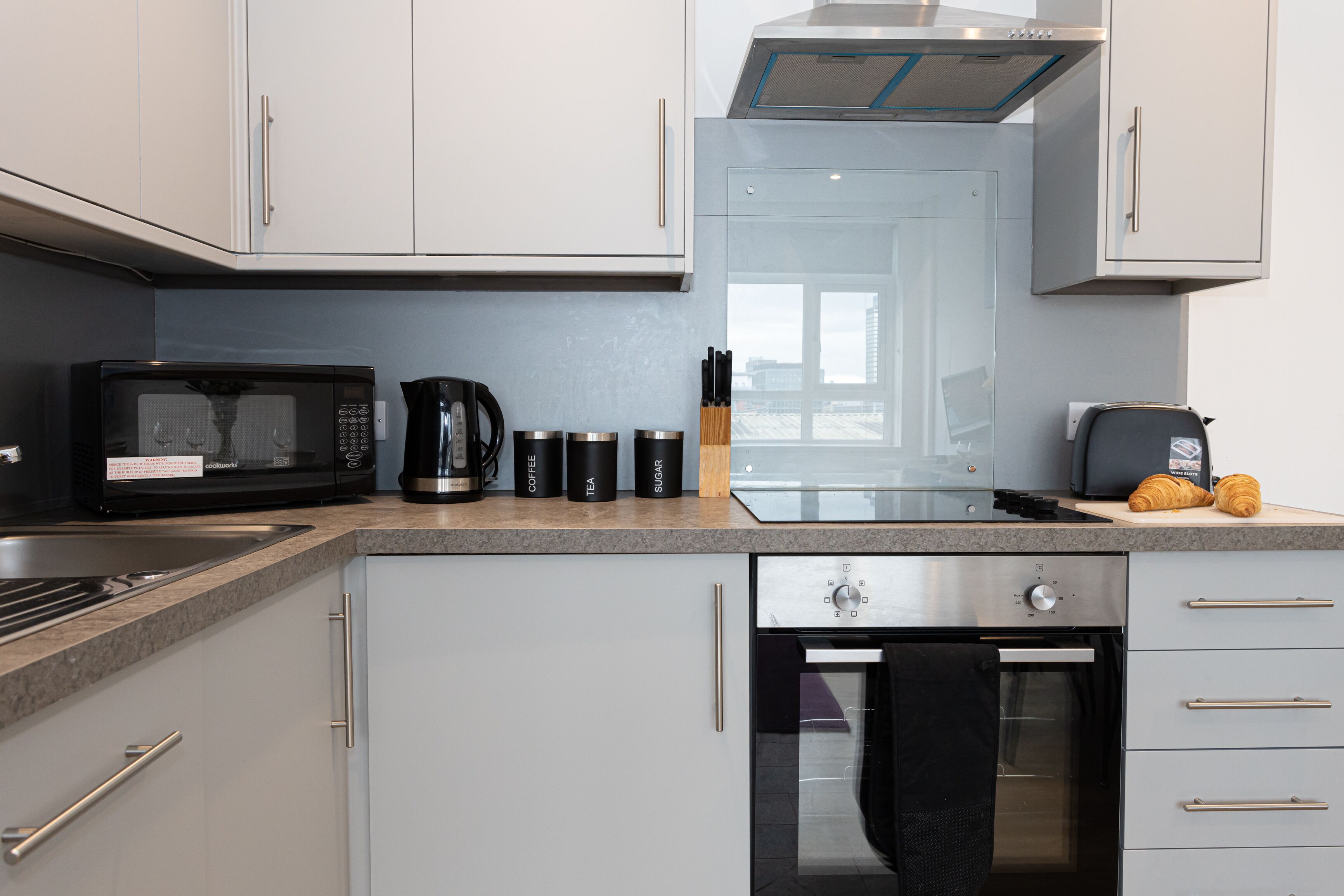 A modern kitchen with a microwave, coffee maker, and toaster. There is a glass door oven and a stainless steel range hood.