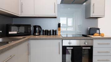 A modern kitchen with a microwave, coffee maker, and toaster. There is a glass door oven and a stainless steel range hood.