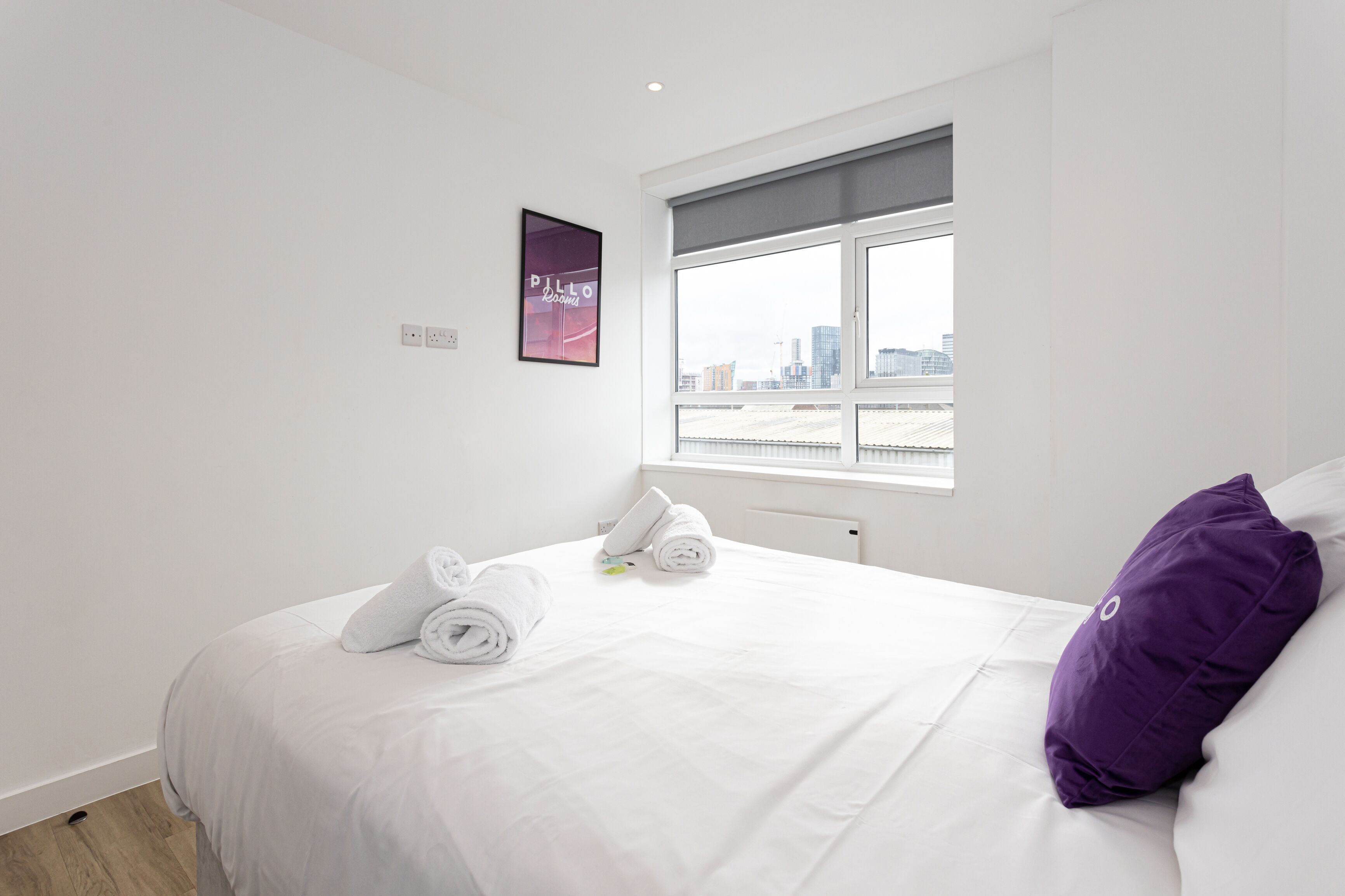 Una camera d'albergo con un letto, una finestra che si affaccia sulla città e un quadro appeso al muro.