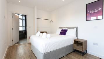 A modern bedroom with a large bed, a bedside table, a hanging light, and a door leading to a bathroom.