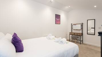 A hotel room with a bed, a desk, a chair, a mirror, and a wall-mounted artwork.