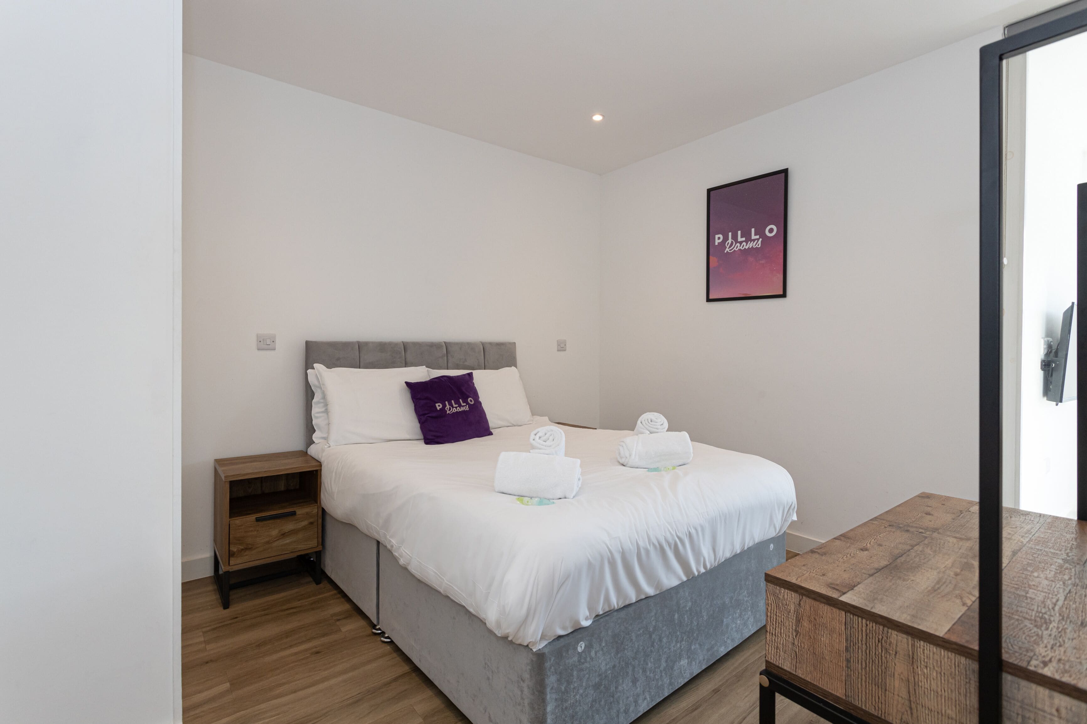 A bedroom with a bed, a nightstand, a wooden table, and a wall-mounted picture.