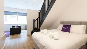 A modern hotel room with a large bed, a staircase, and a view of the outside. - Pillo Rooms Apartments- Manchester Arena (Manchester)