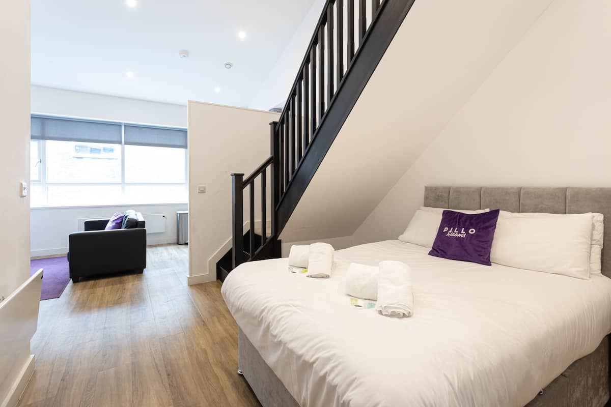 A modern hotel room with a large bed, a staircase, and a view of the outside.