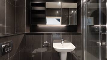 Une salle de bain moderne avec un lavabo blanc, une douche en verre et des murs recouverts de carreaux foncés.