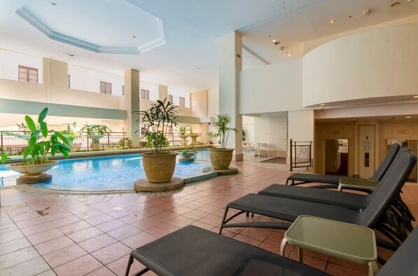 An indoor swimming pool with lounge chairs, potted plants, and a modern architectural design.