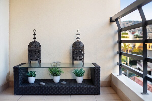 Un balcon avec une table en verre, deux plantes en pot, des lanternes décoratives en métal et une vue sur le paysage urbain.