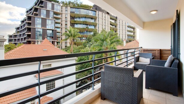 Ein Balkon mit Korbmöbeln, Blick auf ein modernes Gebäude mit Balkonen und einem klaren Himmel.