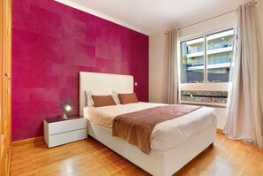 Une chambre à coucher avec un lit, une table de chevet et une fenêtre donnant sur un immeuble.