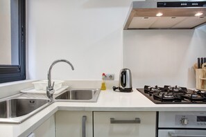 A modern kitchen with a stainless steel sink, a kettle, and a gas stove.