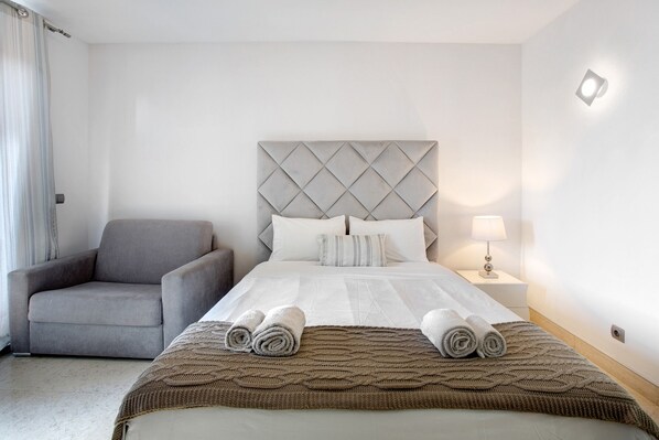 A hotel room with a bed, a chair, a nightstand, and a lamp.