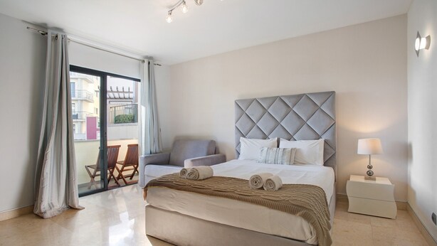 Une chambre avec un grand lit, une table de chevet, une chaise et une vue sur l’extérieur.