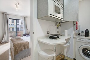 Una habitación de hotel compacta con cama, una kitchenette pequeña, lavadora y vistas al balcón exterior.