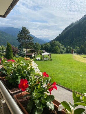 A view of a green lawn with a gazebo, a mountain in the background, and a building with a sloped roof.