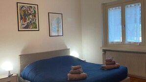A bedroom with a bed, two framed artworks, a window with curtains, a radiator, and a bedside lamp. - Apartment "Casa Nova" with Mountain View & Private Garden (Ponte Rendena)
