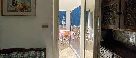 Een geopende deur die leidt naar een balkon met een tafel en stoelen, een schilderij aan de muur en een keuken met kasten.