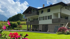 A two-story house with a balcony, a well-maintained lawn, and mountains in the background. - Apartment "Casa Nova" with Mountain View & Private Garden (Ponte Rendena)