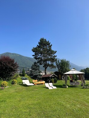 A grassy outdoor area with a gazebo, lounge chairs, and a wooden bench.