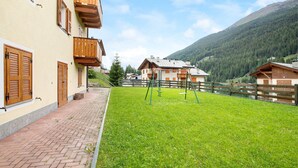 Ein Wohnhaus mit hölzernen Balkonen, einem gepflasterten Weg und einem Rasen mit Schaukeln.