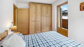 Ein Schlafzimmer mit einem Bett, einem Holzschrank, einem Fenster und einer Tür.