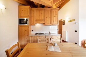 A kitchen with wooden cabinets, a microwave, a stove, and a dining table with chairs. - Apartment 'Casa Michela Trilocale Mansardato' with Mountain View, Shared Terrace and Wi-Fi (Valfurva)