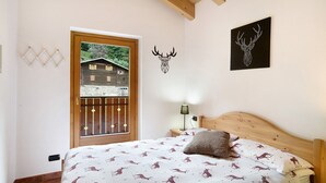 Una camera da letto con un letto, una testata in legno, un comodino con una lampada, una decorazione a testa di cervo appesa al muro e una finestra vista su un edificio.