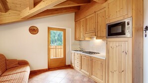 Une cuisine compacte avec des meubles en bois, un four à micro-ondes encastré et une fenêtre donnant sur un espace verdoyant.