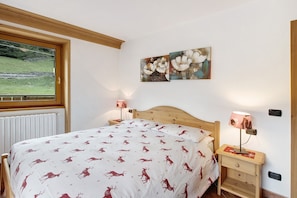 A bedroom with a bed, a nightstand, a lamp, and two paintings on the wall.