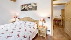 Ein Schlafzimmer mit einem Bett, zwei Nachttischlampen, einem Nachttisch, einer Holztür und einem Essbereich mit Tisch und Stühlen.