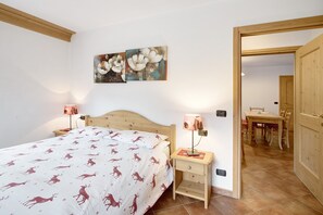 Une chambre à coucher comprenant un lit, deux lampes de chevet, une table de nuit et une porte en bois, ainsi qu’un coin repas avec une table et des chaises.