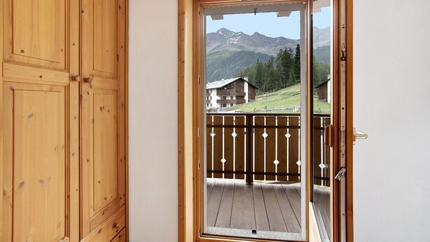 Eine Holztür führt zu einem Balkon mit Blick auf Berge und Häuser.