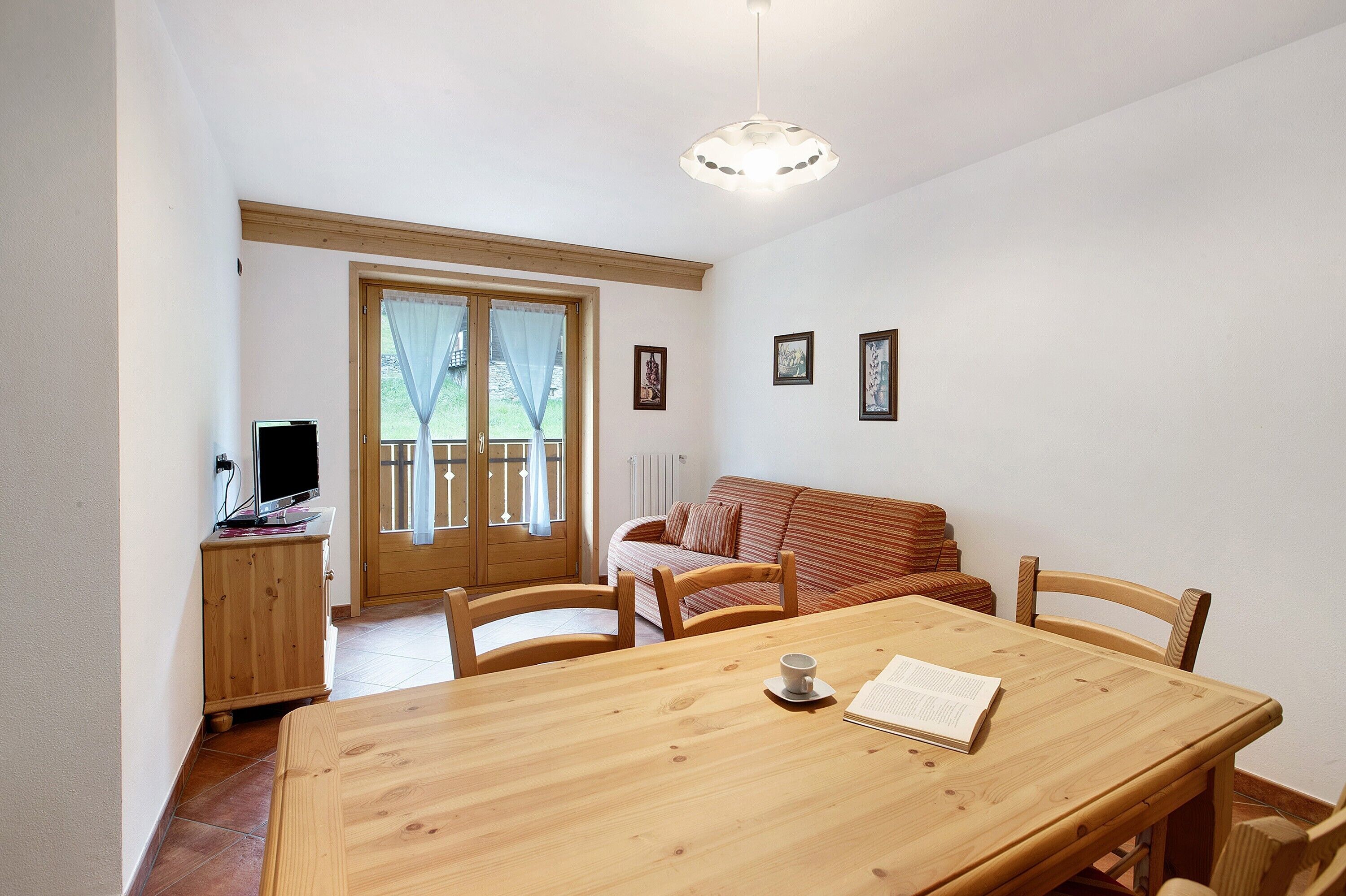 A dining area with a wooden table, chairs, a television on a stand, and a sofa.