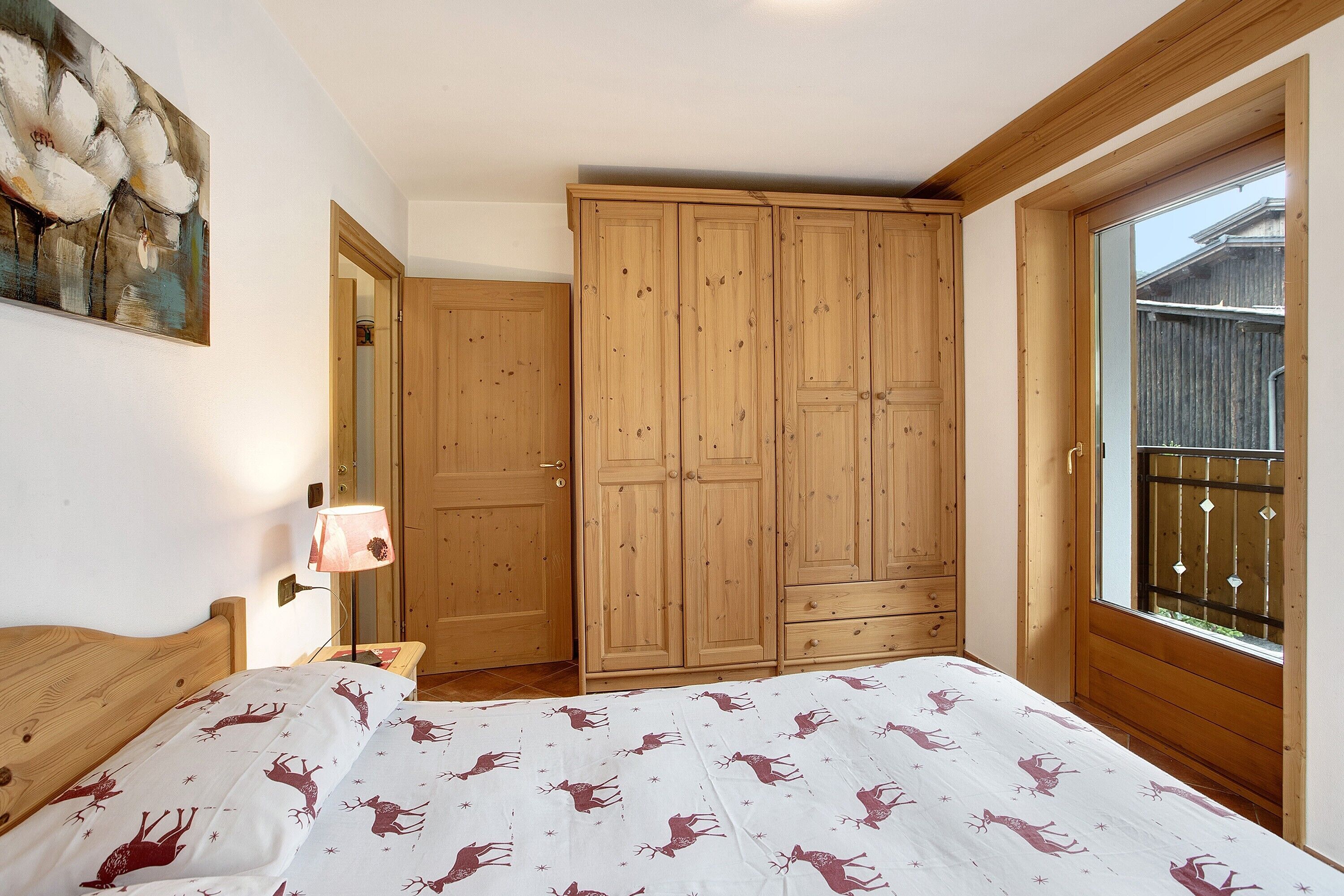 Een slaapkamer met een bed, een houten garderobe, een raam met uitzicht en een schilderij aan de muur.